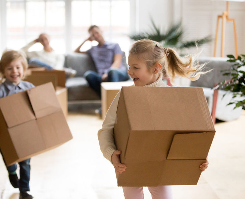 Two children holding boxes as their parents look on from the couch