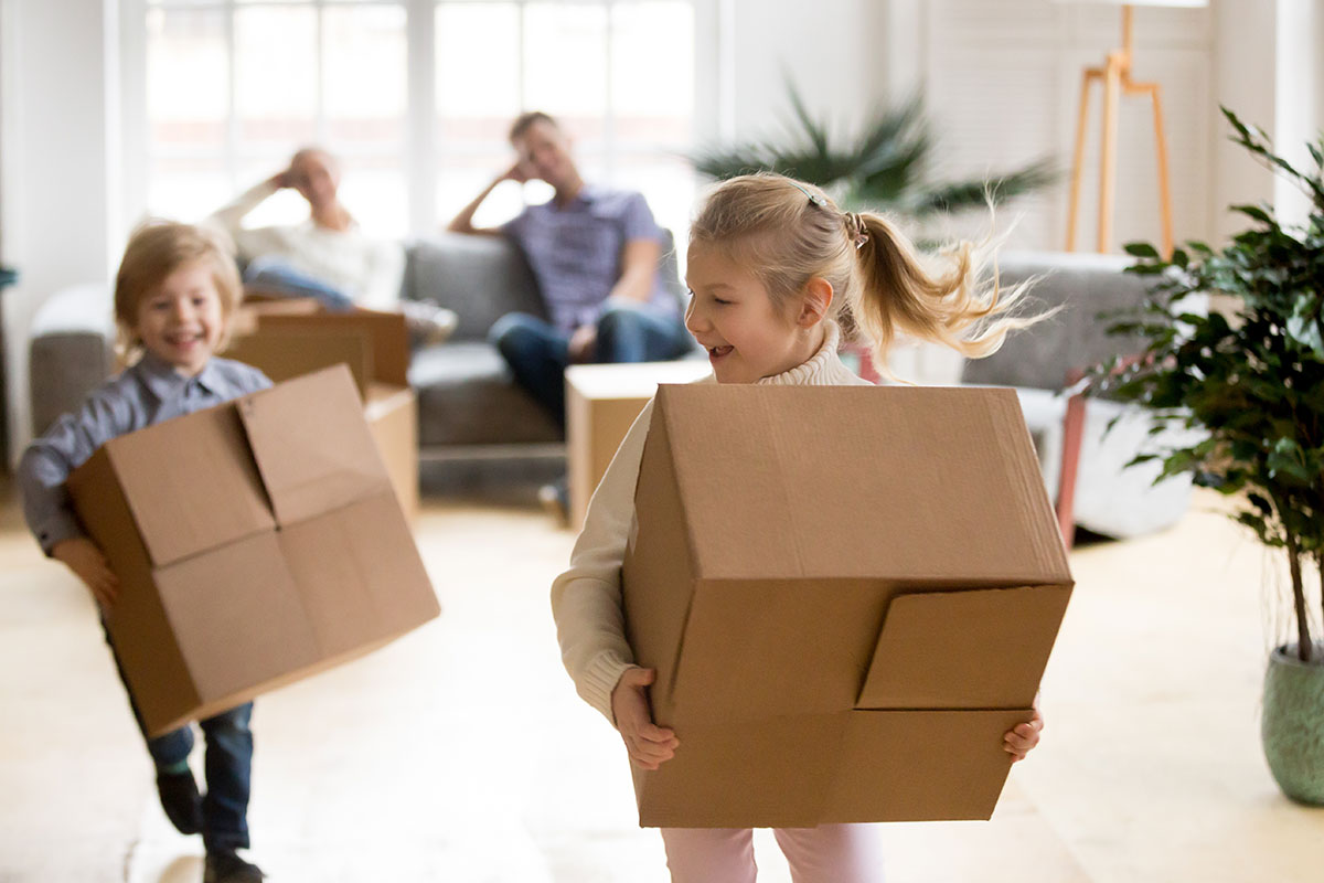 Two children holding boxes as their parents look on from the couch